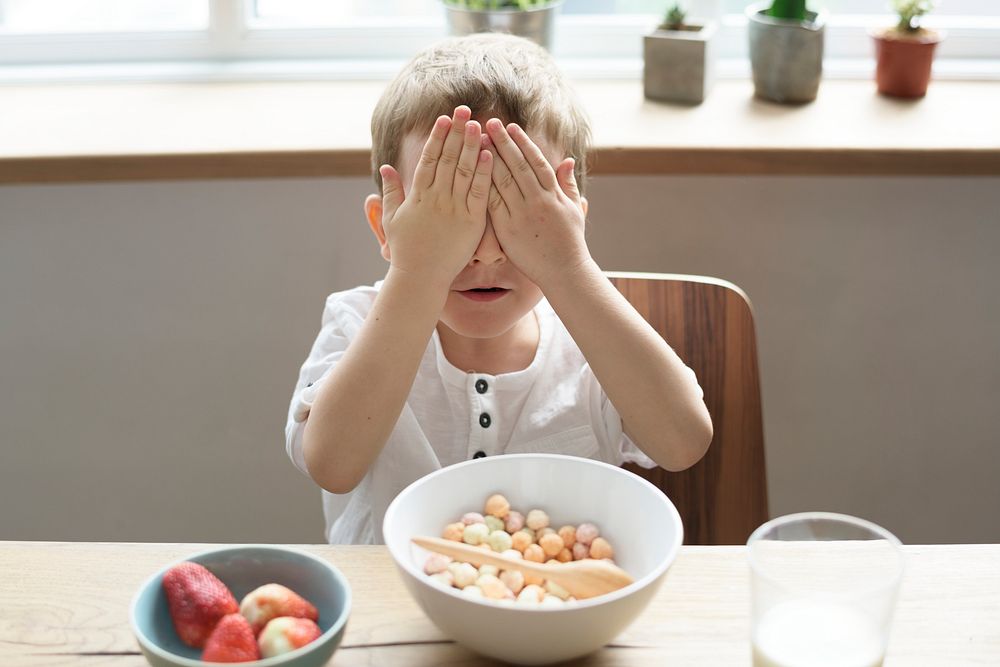 Little boy covering his eyes while having breakfast