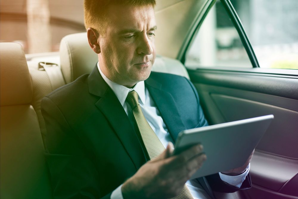 Businessman using digital tablet on backseat of the car