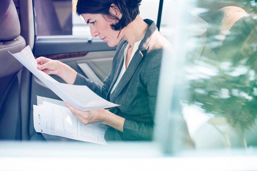 Businesswoman reading documents on backseat of the car