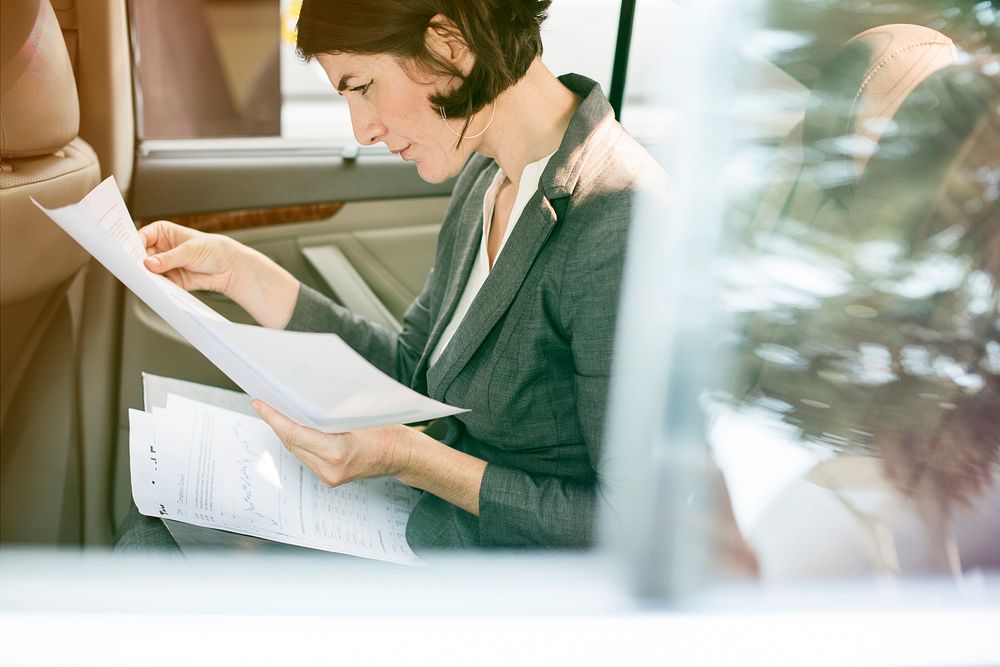 Businesswoman reading documents on backseat of the car