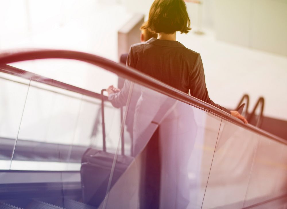 Businesswoman traveling with luggage on escalator