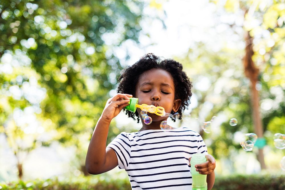 African descent kid enjoying blowing bubble outdoors