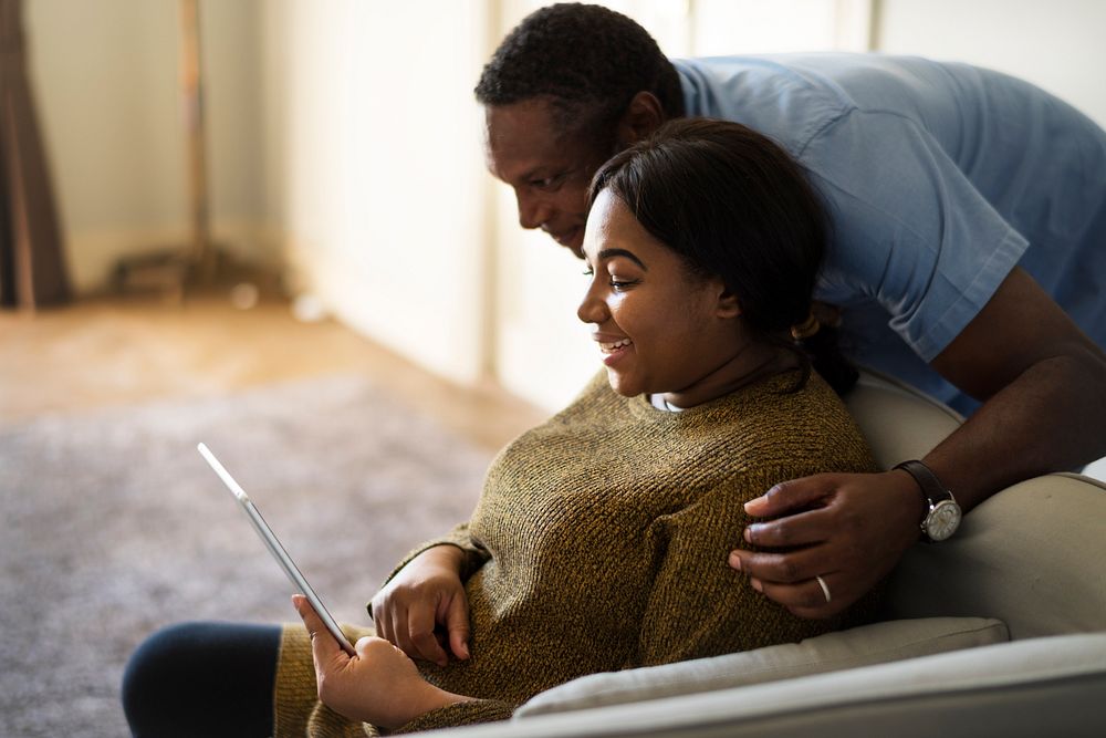 African descent husband and wife resting at home, using a tablet together