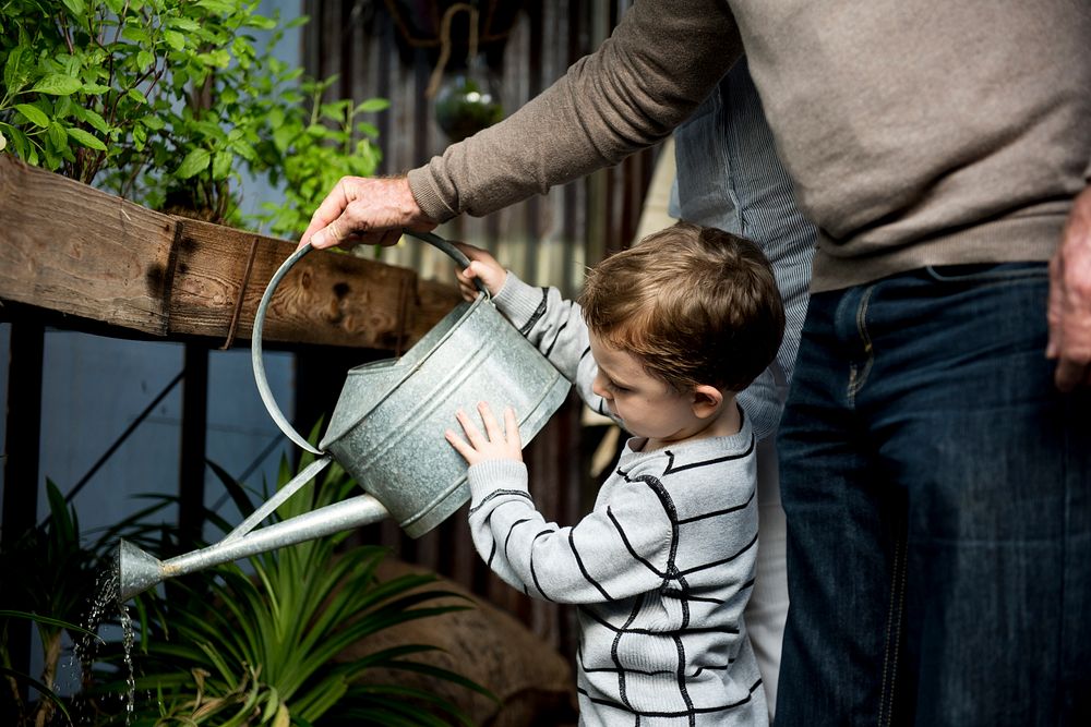 Man helping a young boy water the plants