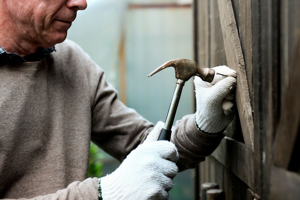 Elderly man fixing a wooden door with hammer