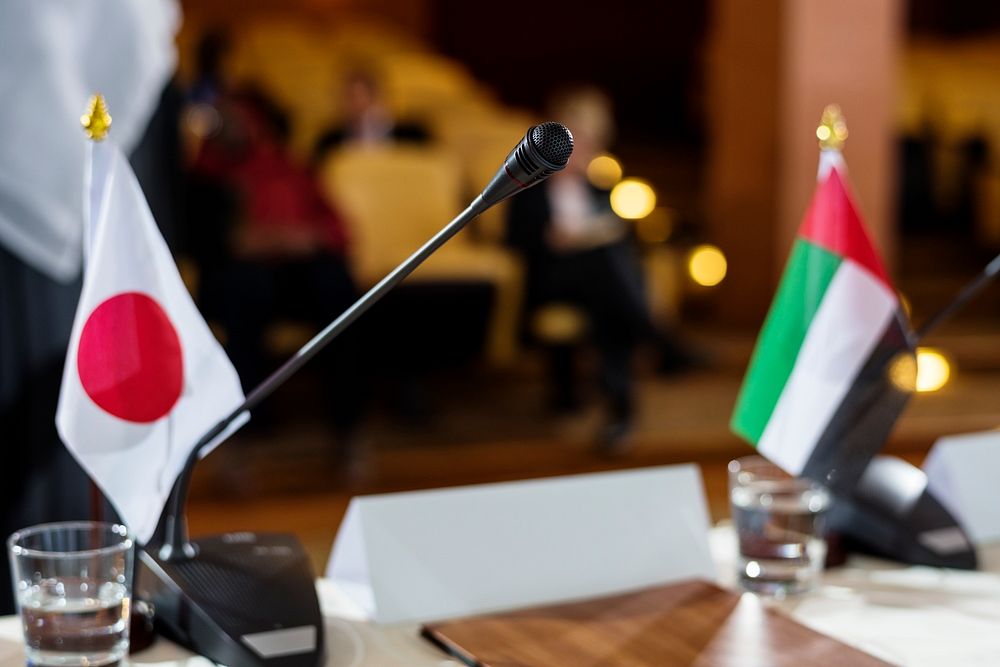 Japanese and Emirati Flags on a Table with Microphone in an International Conference 