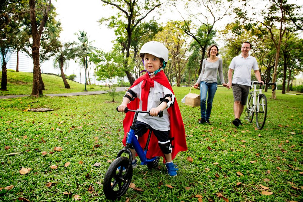 Superhero boy riding his bicycle through the park