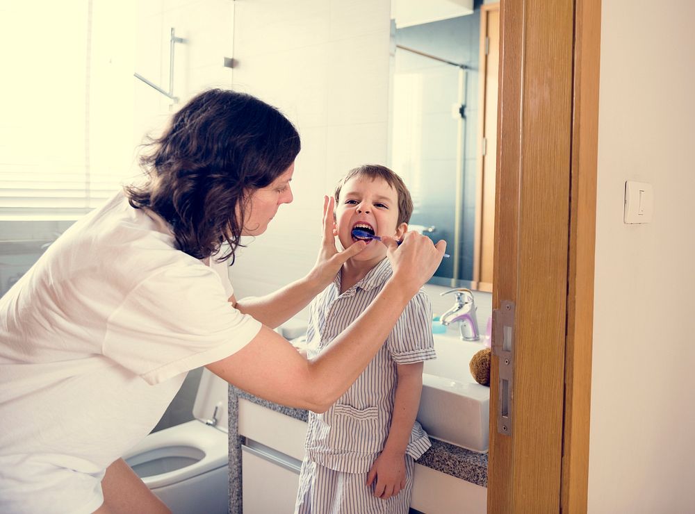 Mother teaching and helping the son how to brush his teeth