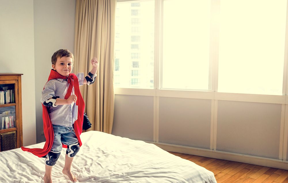 Playful superhero little boy jumping on the bed