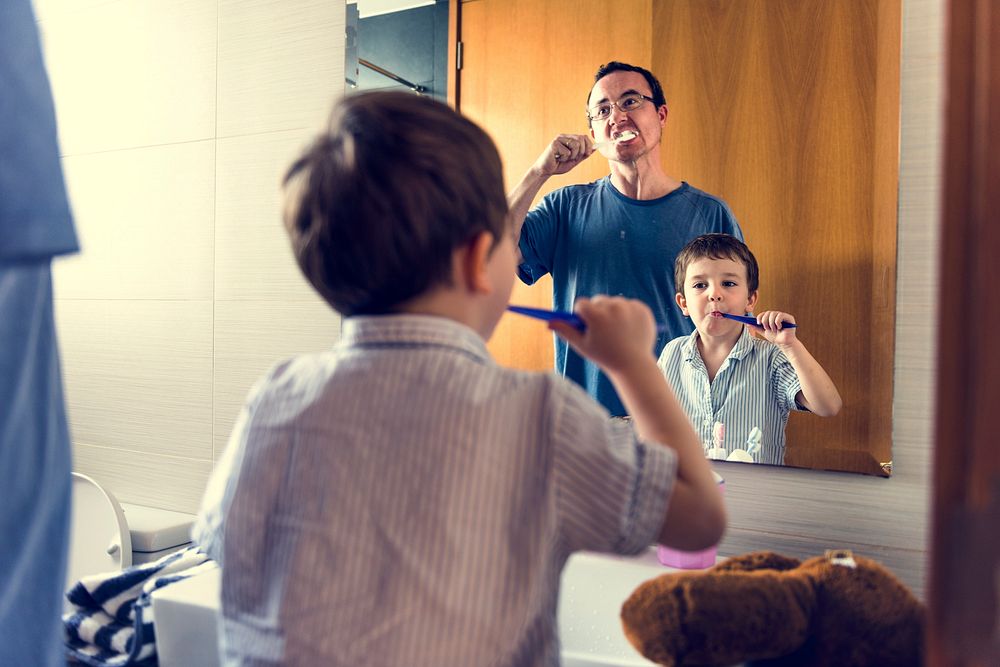 Father teaching the son how to brush his teeth