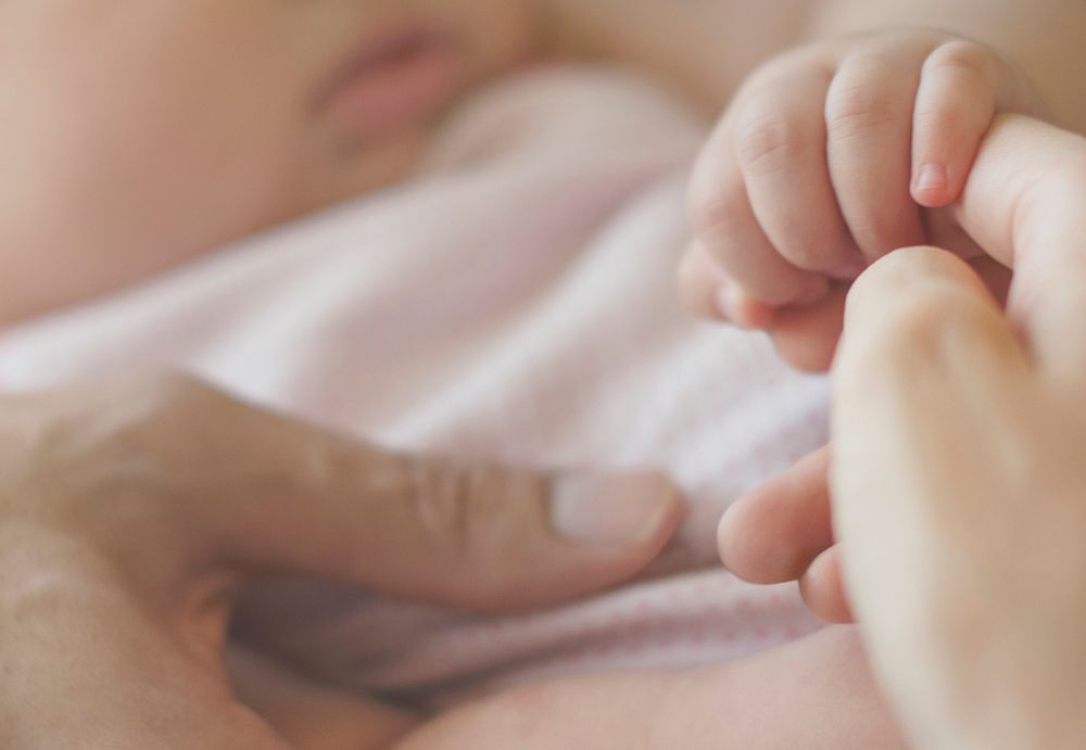 Closeup of baby holding mother hands