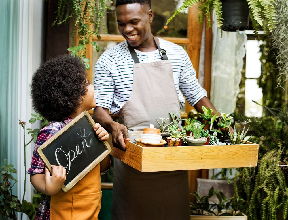 Man Carrying Plants Standing With Son Showing Open Sign