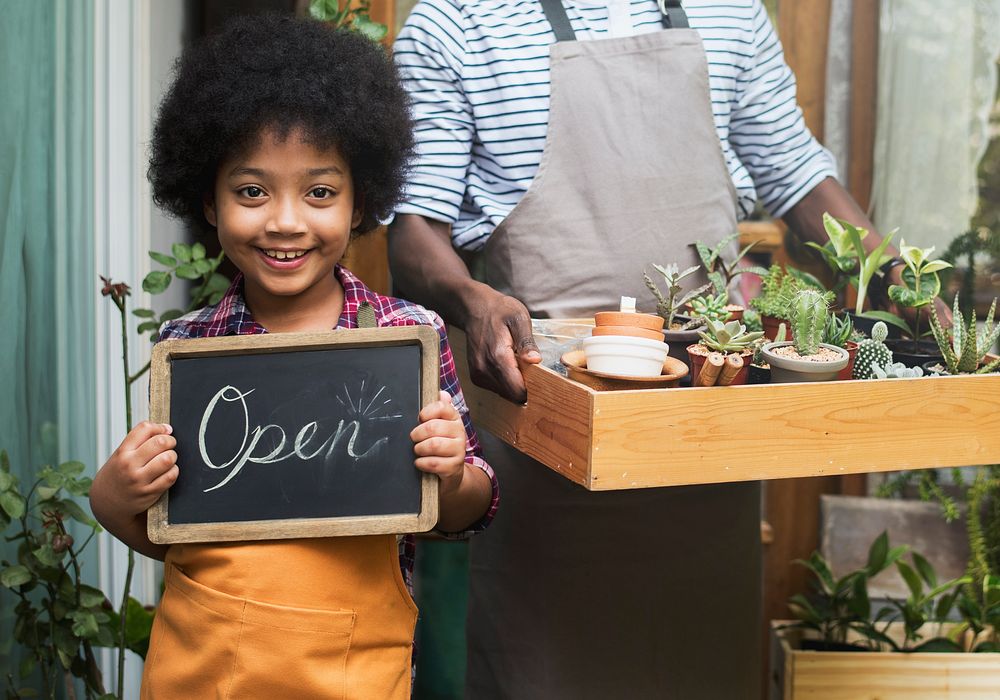 Man Carrying Plants Standing With Son Showing Open Sign