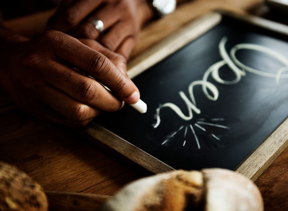 Closeup of hands writing open word on chalkboard