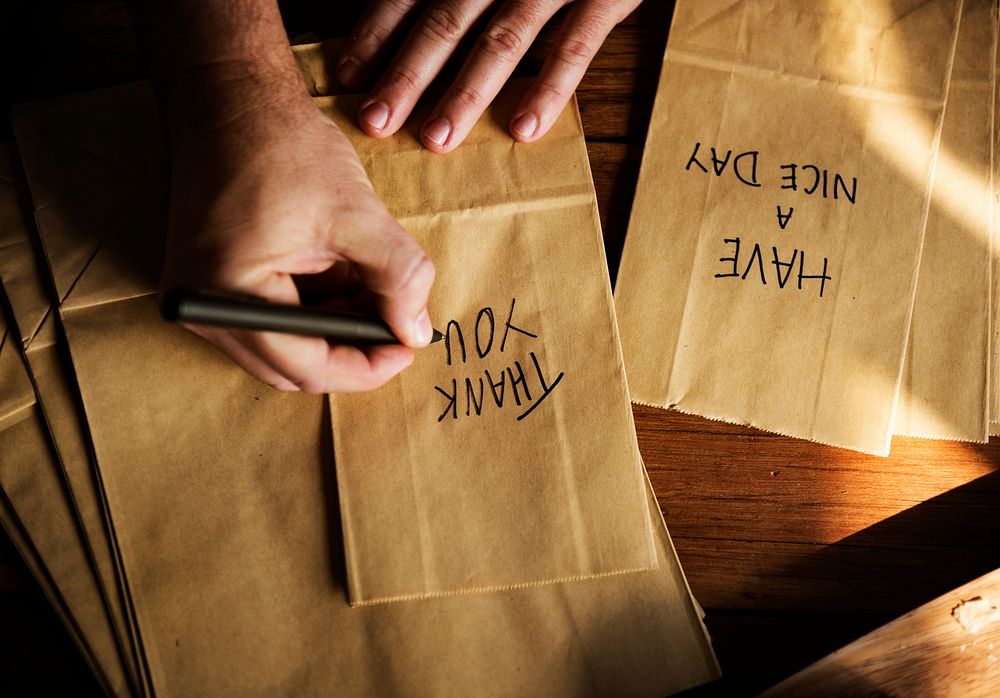 Hands Writing Thankful Words on Paper Bags