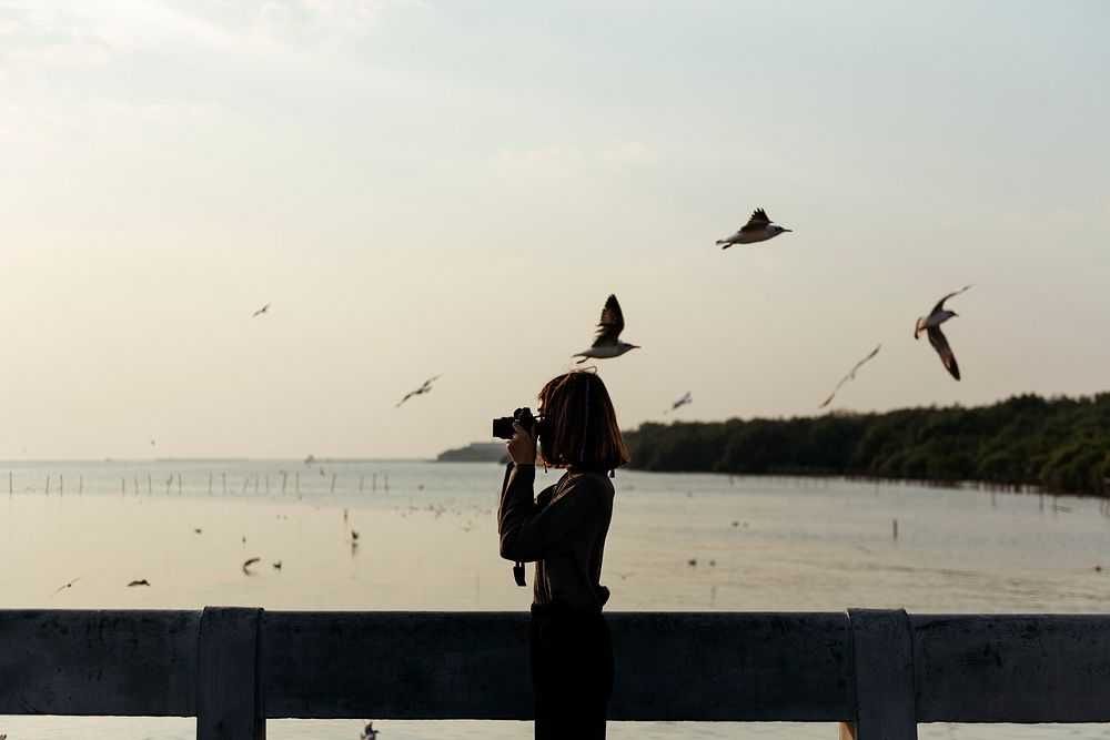 Girl taking photos of birds flying above the ocean