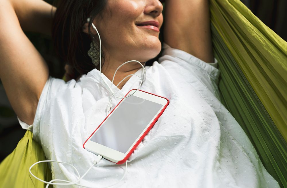 Woman using smart phone with earphone laying on hammock