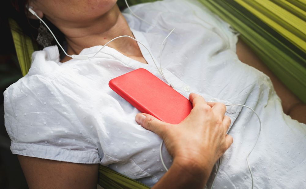 Woman using smart phone with earphone laying on hammock