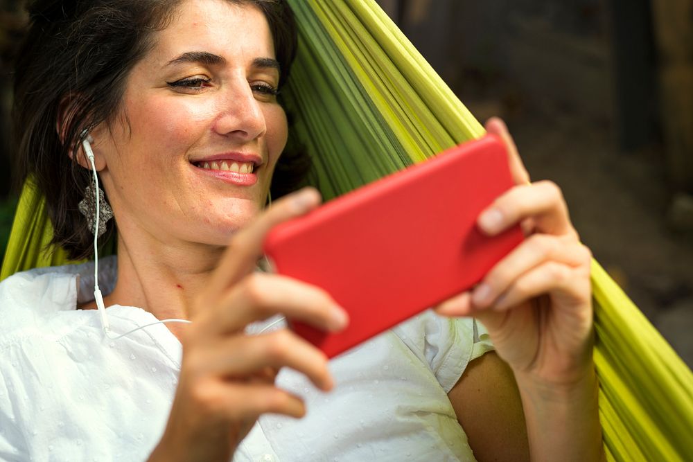 Woman using smart phone with earphone laying on hammock