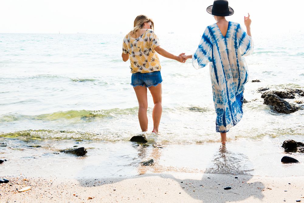 Girlfriends holding hands and walking on the beach