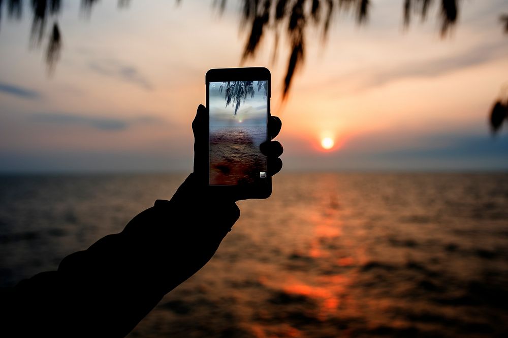 Hand taking a photo of the sunset with phone camera