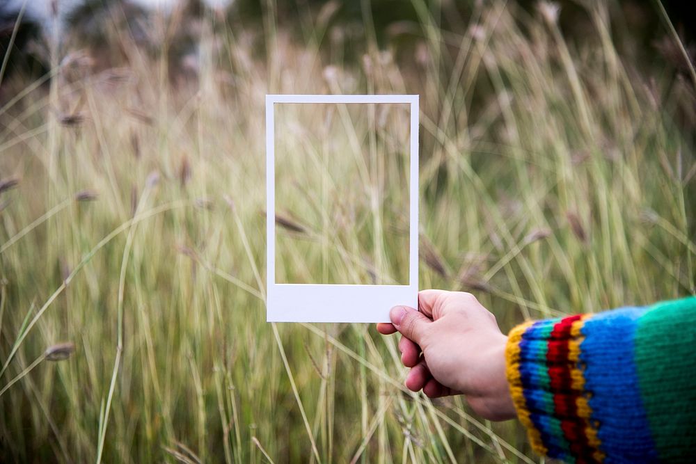 Hand holding a photo frame border to the grass field