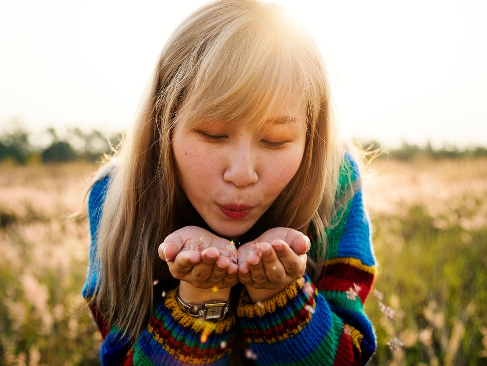 Asian woman blowing flower petals off her hands