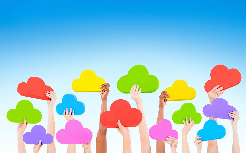 Hands holding multi colored cloud shaped speech bubbles with blue sky.