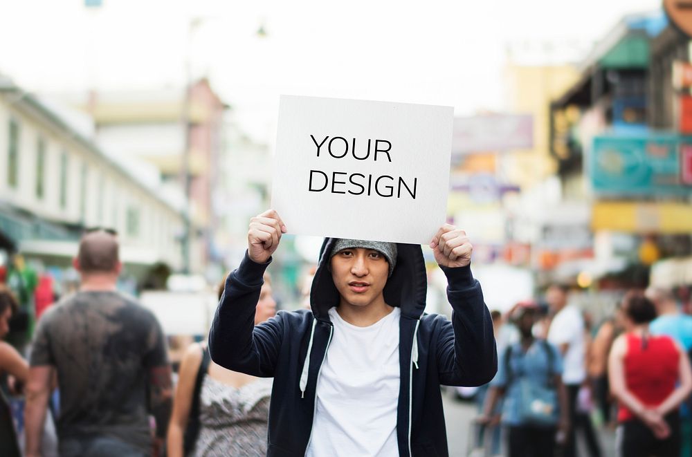 Young asian man holding empty placard outdoors