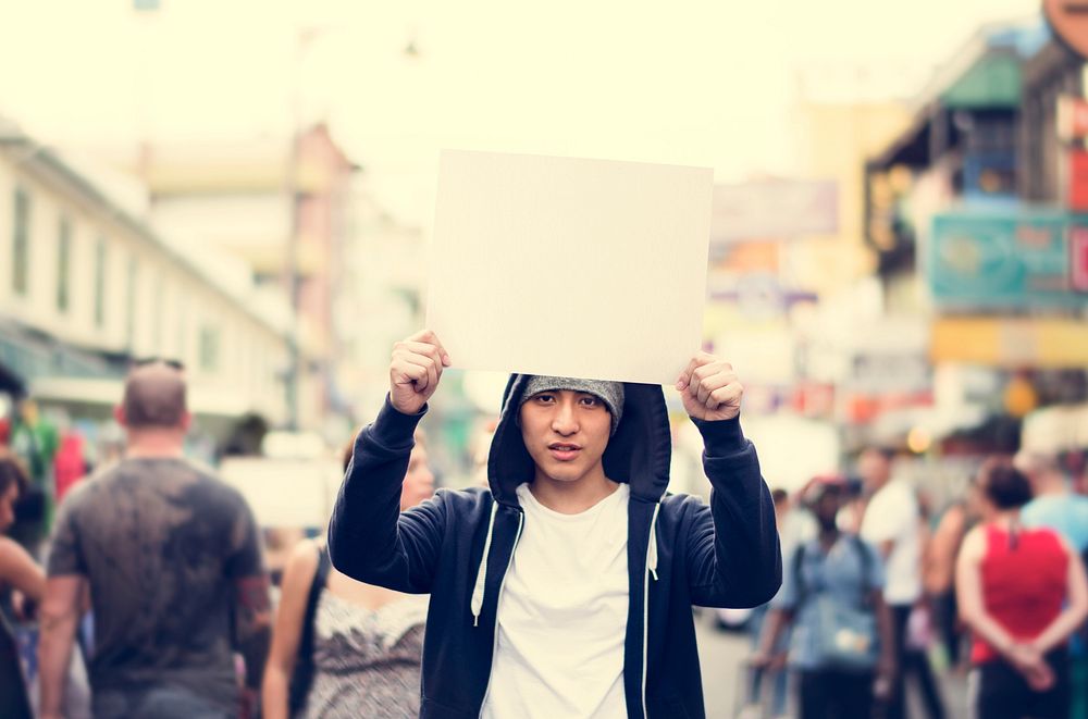 Young asian man holding empty placard outdoors
