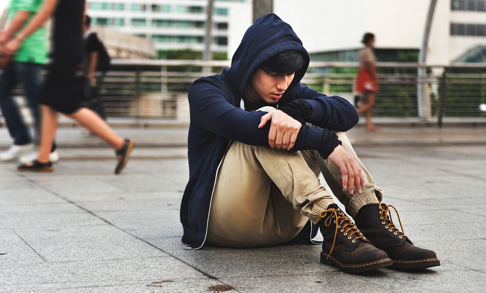 Distressed guy in a hoodie sitting outdoors