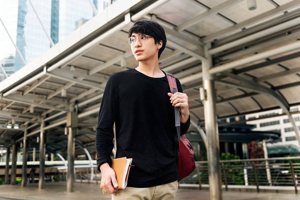 Asian man holding notebook and walking in the city