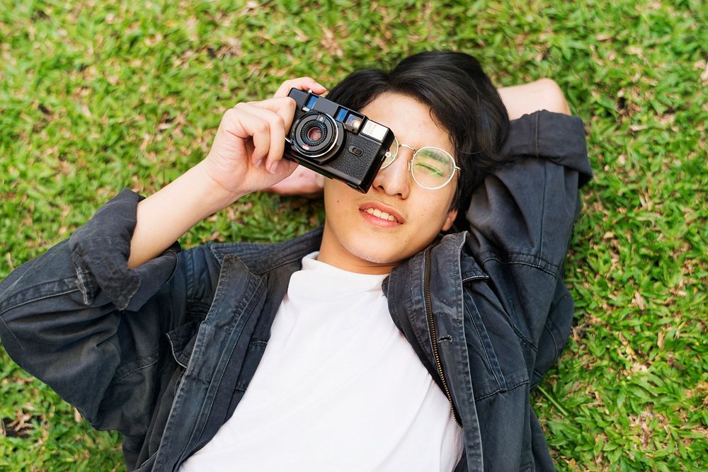 Young asian boy taking a photo while lying on the grass