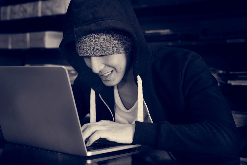 hacker in hoodie using laptop for cyber crime