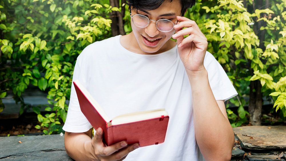 Young guy reading a book outdoors
