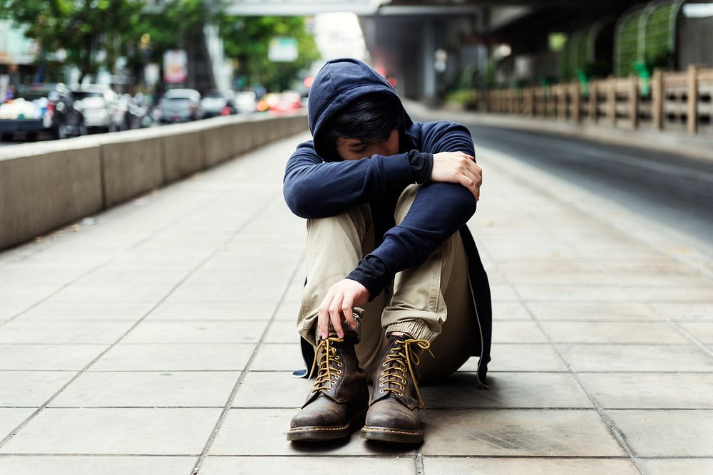 Lonely man sitting on the ground in urban scene