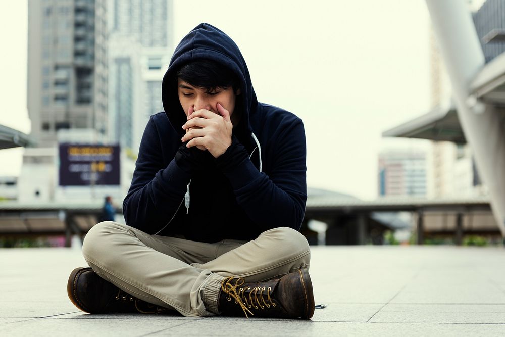 Lonely man sitting on the ground in urban scene