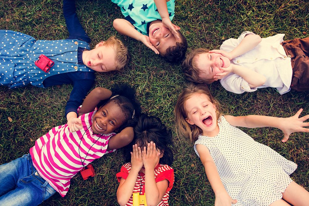 Group of kindergarten kids lying on the grass at park and relax