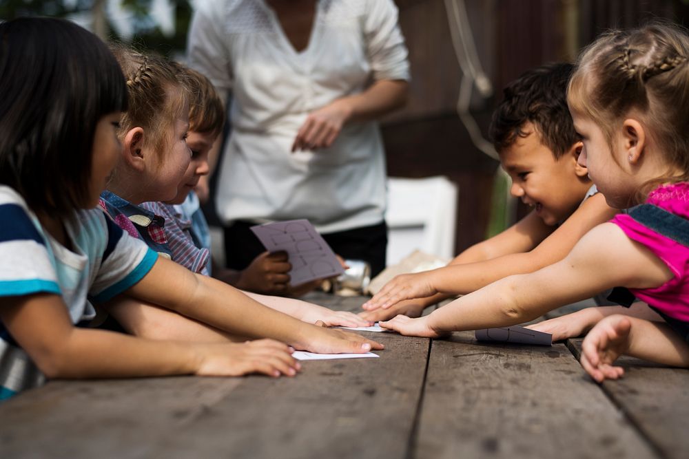 Group of children reaching for paper on wooden table