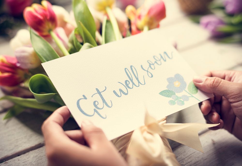 Hands HoldingGet Well Soon Wishing Card with Tulips Flowers as Background