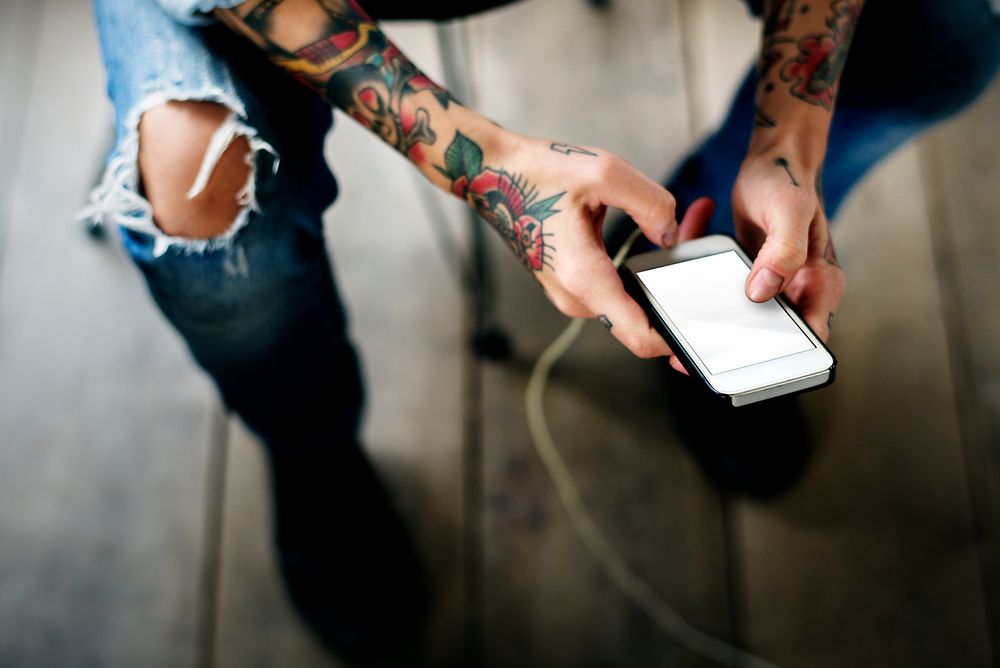 Close up of tattooed hands using mobile phone
