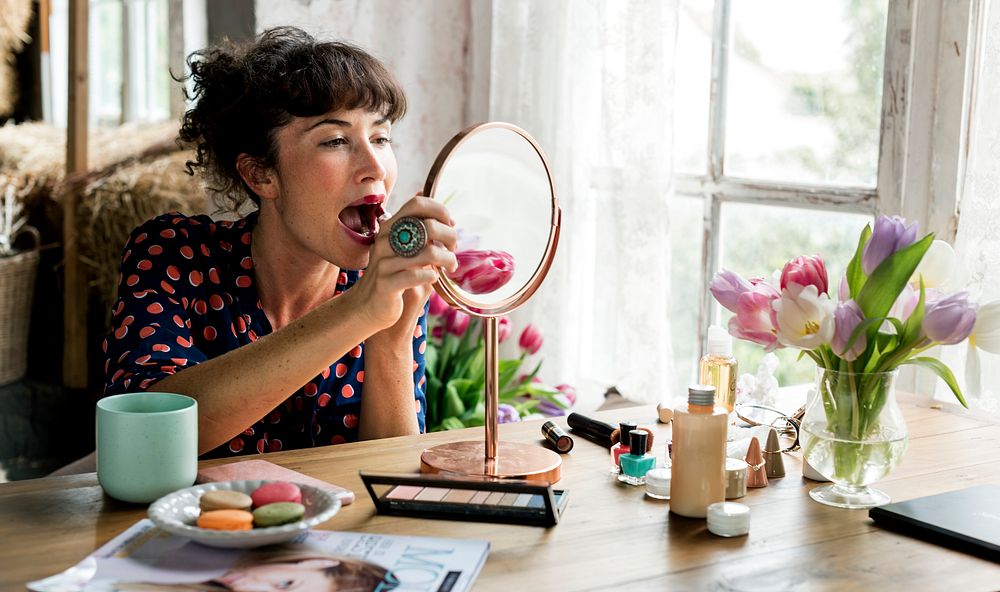 Woman putting on lipstick with a mirror