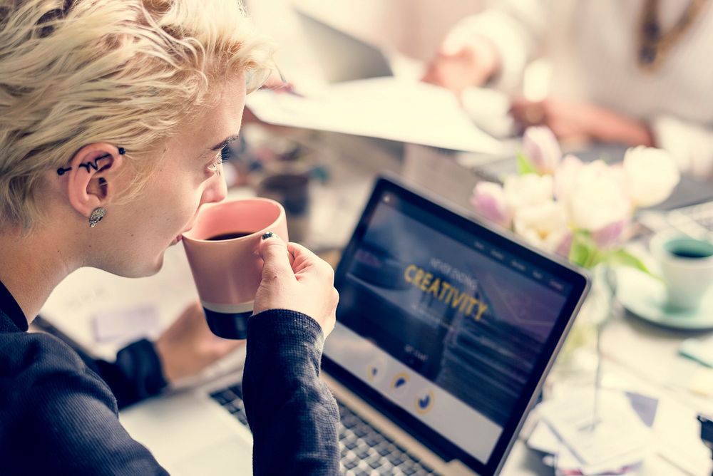 Woman Sipping Coffee while Working on Laptop
