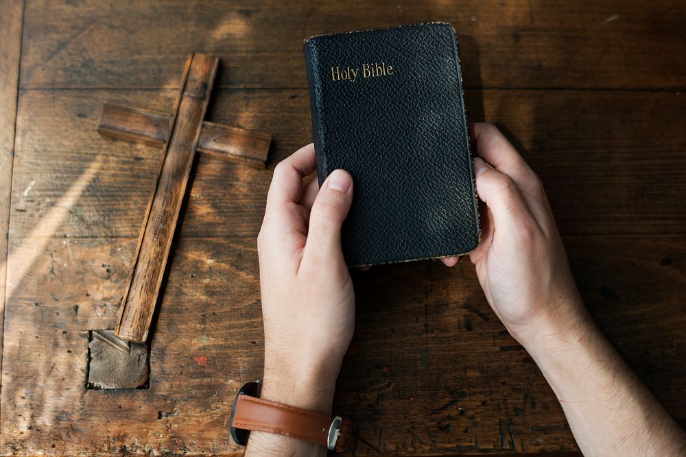 Hands Holding Holy Bible with Wooden Cross
