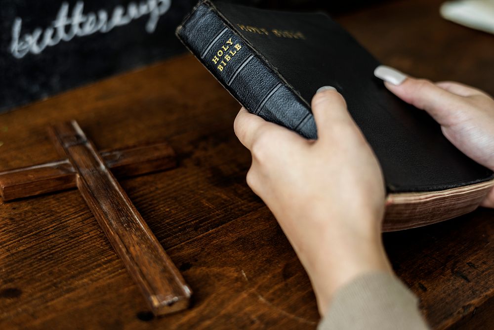 Female hands holding a bible and a wooden cross