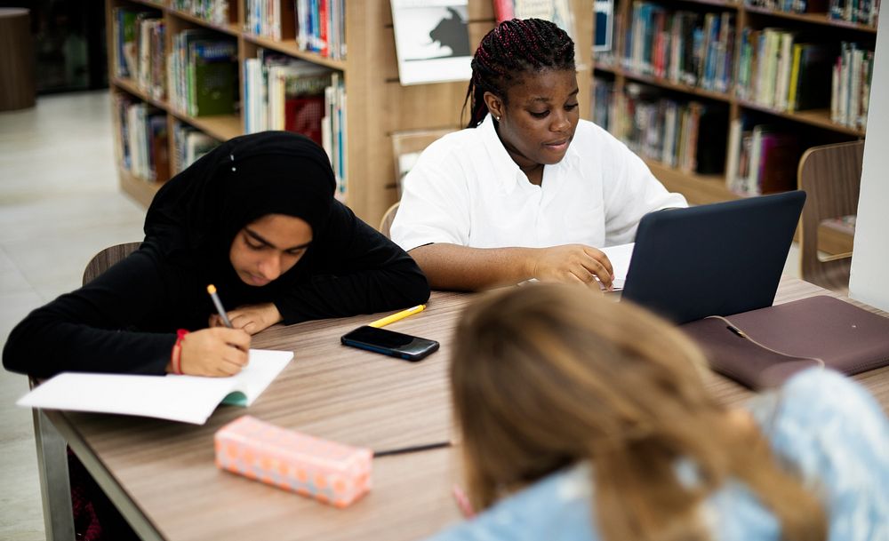 Diverse group of high school student studying doing homework in library