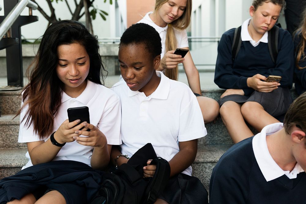 Group of students sitting at stairs and using digital devices