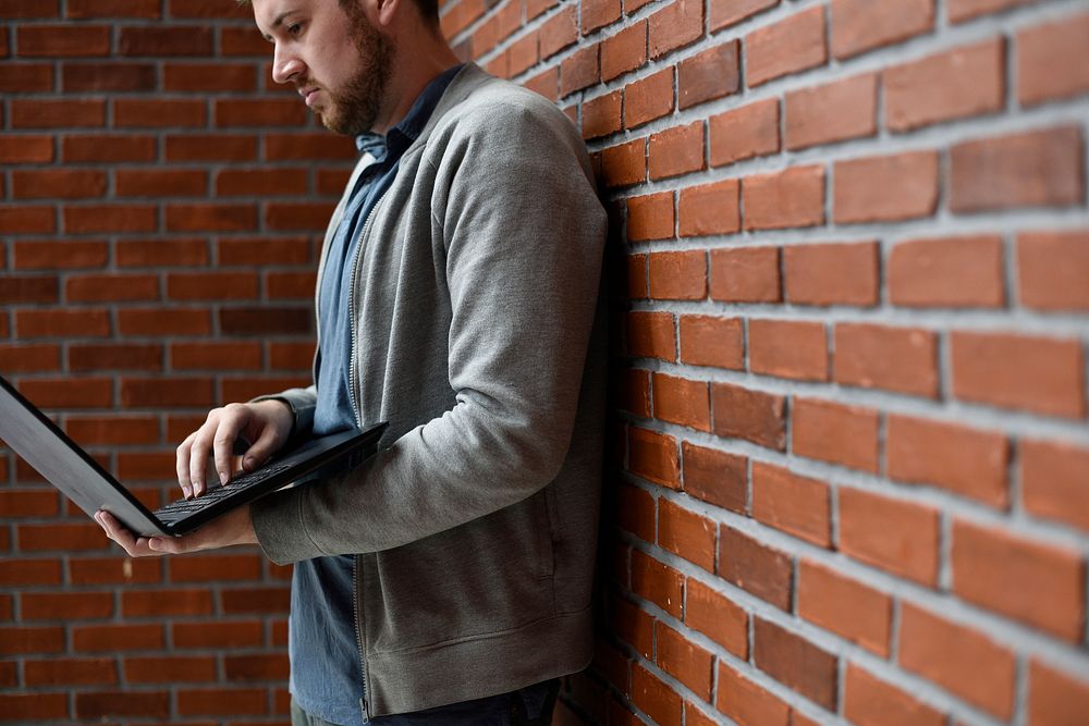 Man lean on brick wall and using laptop