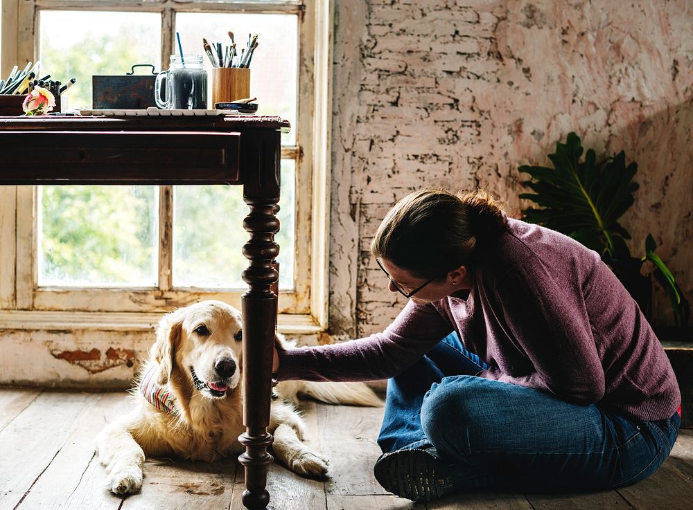 Caucasian woman sitting on wooden floor petting golden retriever dog