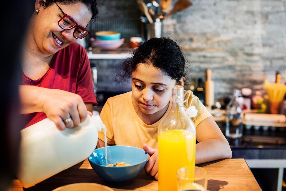 Mom pouring milk in daughter's cereal